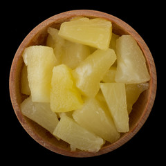 pieces of pineapple  in wooden cup isolated on black background. top view