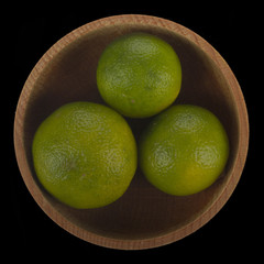  heap of limequates  in wooden cup isolated on black background. top view