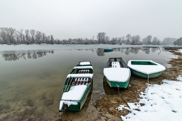 Naklejka premium Danube island (Šodroš) near Novi Sad, Serbia. Colorful landscape with snowy trees, beautiful frozen river. A boats covered with snow or submerged