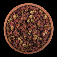Sichuan pepper in wooden cup isolated on black background. top view