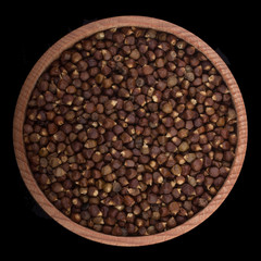 Grains of paradise  in wooden cup isolated on black background. top view