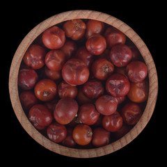 red juniper berries  in wooden cup isolated on black background.  top view