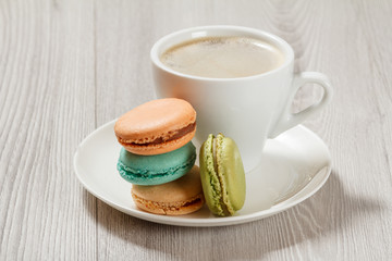 Obraz na płótnie Canvas Cup of coffee and delicious macarons cakes of different color on white plate