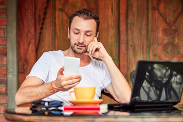 Man with smartphone, coffee / tea and laptop on a home porch.