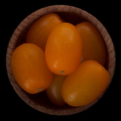 orange tomatoes in wooden cup isolated on black background.  top view