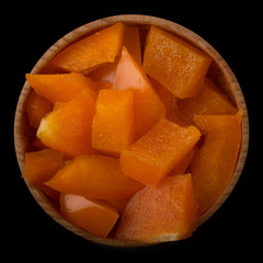 slices of orange pepper in wooden cup isolated on black background.top view