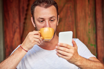 Man with smartphone, coffee / tea on a home porch.