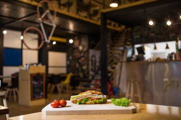 An appetizing sandwich on a wooden board with vegetables.