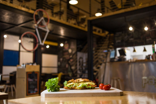 An appetizing sandwich on a wooden board with vegetables.