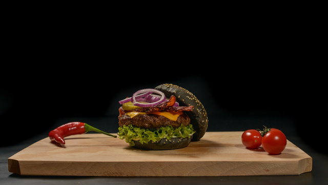 An appetizing black hamburger on a wooden board with fresh vegetables.