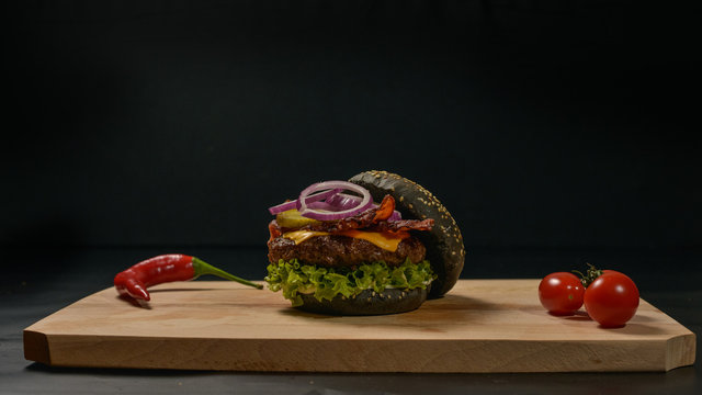 An appetizing black hamburger on a wooden board with fresh vegetables.