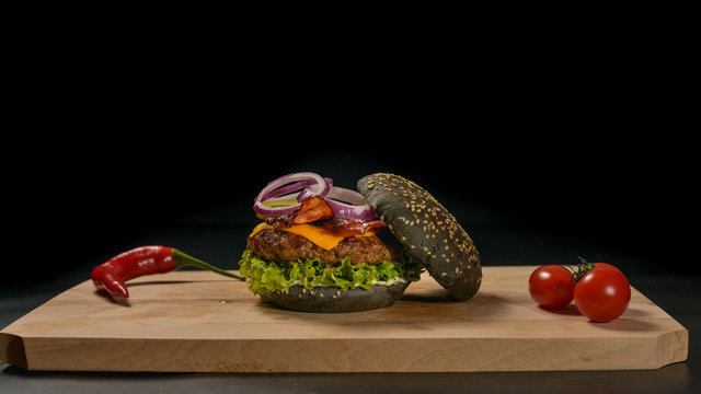 An appetizing black hamburger on a wooden board with fresh vegetables.