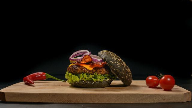 An appetizing black hamburger on a wooden board with fresh vegetables.