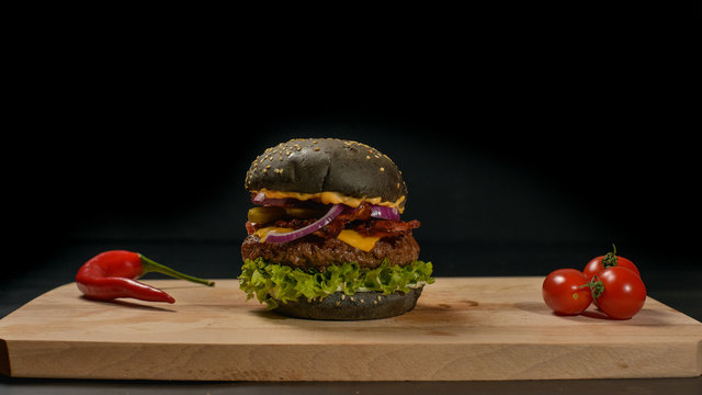 An appetizing black hamburger on a wooden board with fresh vegetables.