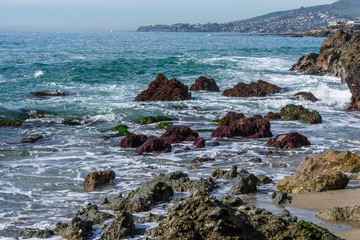 Fototapeta na wymiar Azure waves crashing over colorful rocks in California