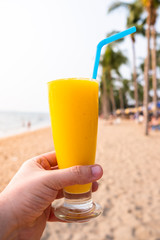 Mango fruit juice hold hand, background is tropical island