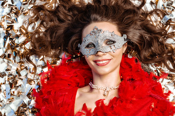 Mystical young woman lying on the floor among the golden tinsel, smiling close-up wearing a carnival mask