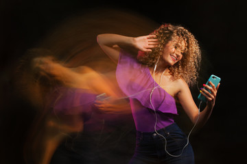 Attractive dancing woman with curly hair and red headphones in black background, neon light, motion effects. Copyspace, long exposure.