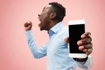 Indoor portrait of attractive young black african man isolated on pink background, holding blank smartphone, smiling at camera, showing screen, feeling happy and surprised. Human emotions, facial