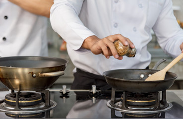 Two handsome chefs in white uniform are talking to each other while cooking in kitchen or...