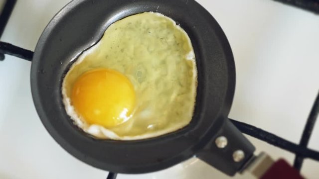 Cooking a fried egg in a mini pan in the shape of a heart for Valentine's Day. Slow motion shot