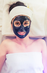 Close up of Healthy Young Woman getting mud Black facial mask cosmetic procedure in the beauty salon.Skin treatment in spa salon concept
