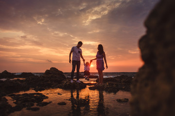Fototapeta premium Mama, tata i syn. Rodzina spaceruje po kamienistej plaży nad morzem.