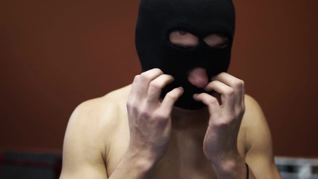 Boxer or fighter topless put on the thief, rubber mask while standing on the boxing ring in the gym