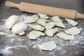 Fototapeta na wymiar Uncooked dumplings on a metal table with white mushrooms champignons and a rolling pin