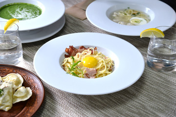Delicious pasta with bacon, egg and parmesan cheese on the table with soup, dumplings and water with lemon for business lunch 