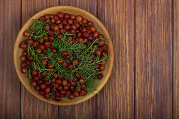 heap of red juniper berries in wooden plate on wooden background. top view