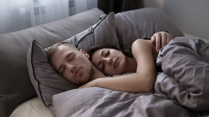 Portrait of young caucasian couple sleeping in the bed at home on the grey bed sheets. Morning time