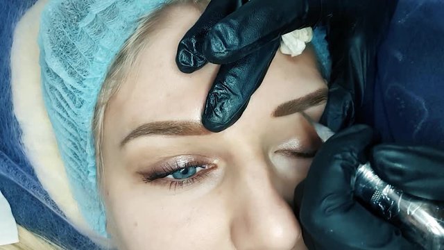 Beautician female applies permanent makeup on eyebrows, tattoo eyebrows on beautiful models in a beauty parlor
