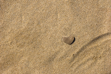 Fototapeta na wymiar A small stone in the form of heart lies on the sand.