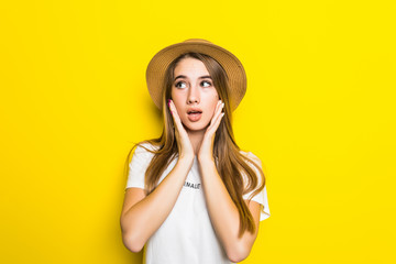 Portrait of shocked fun crazy young woman in straw summer hat, orange glasses put hands on face, copy space isolated on yellow background. People sincere emotions, lifestyle concept.