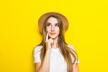 Young pretty Woman thinking in straw hat on yellow background