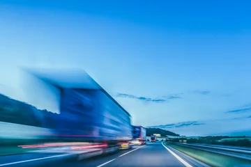 Foto op Plexiglas Snelweg bij nacht Achtergrondfoto van een snelweg. Vrachtwagen op een snelweg, bewegingsonscherpte, lichtsporen. Avond- of nachtopname van vrachtwagens die logistiek en transport doen op een snelweg.