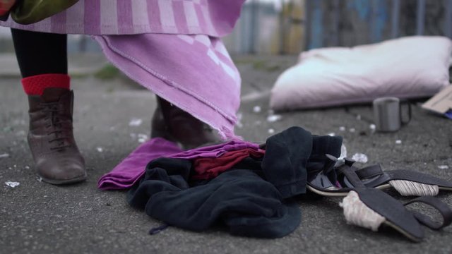 Homeless rummaging in clothes scattered on the street. Close up.