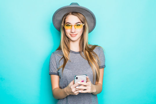 Young smiling woman is using smartphone wearing fluppy hat on blue background
