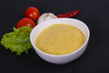 Raw couscous in the bowl served salad leaves, tomato and pepper