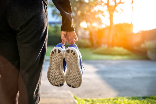 senior Woman in black sportware holding her sport shoes in hands , coming back home after exercise walking in the morning; ; on sunlight the background - Image