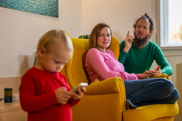 Infant son typing on cell phone with angry parents in the background.