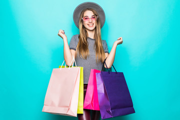 Pretty young woman stylishly dressed in a floppy hat with bags after shopping isolated on blue pastel background