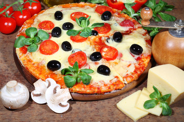 Pizza with olives, mozzarella and ham on a wooden table