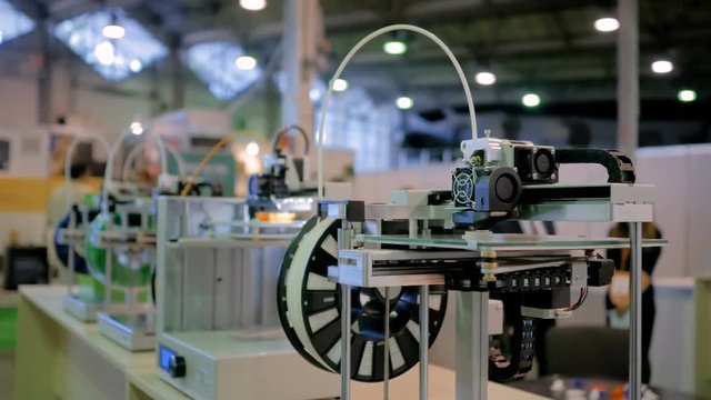 3D printing technology concept - three dimensional printing machines in row making physical 3D model at modern technology exhibition