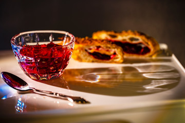 Tea spon with two sliced peaces of the cake with red jam inside covered by sugar  and  saucer with raspberry in blur as background. This picture made by middle format camera.