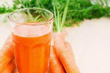 Fresh carrot juice in glass on wooden table background.