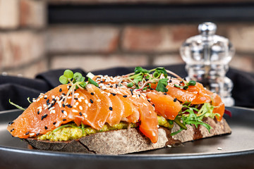 Close up view on sandwich with salmon, microgreen and avocado on a black plate. Healthy food for menu. Free copy space. Healthy diet background