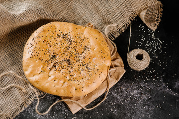 Fresh big rounded flat bread on fabric on the black wooden background