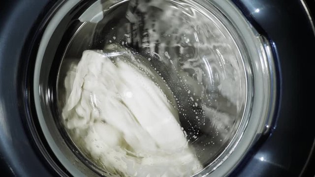 Washing machine washes white clothes. Close-up slow motion shot. Cylinder spinning. Nobody